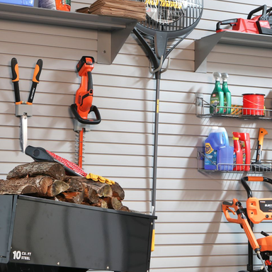 Garage slatwall with racks and hooks from the front with hooks holding clippers, rakes and more.