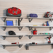 Whitewood slatwall panels with mounted metal shelves holding garage tools, gear, and accessories, showcasing Oura Decor’s organized storage system.