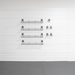 Four black metal wire shelving units of varying lengths mounted on a white paneled wall, with a gray floor below.