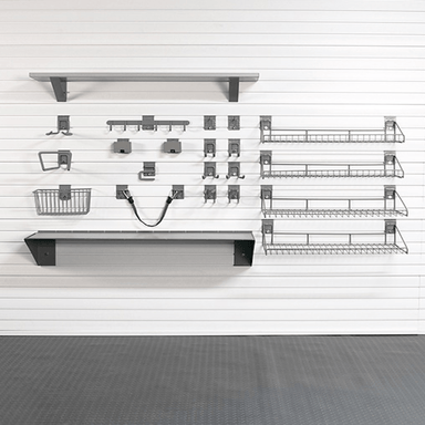 A set of dark gray metal wall-mounted shelves, baskets, and hooks arranged on a white slatwall in a clean indoor setting with a gray floor.