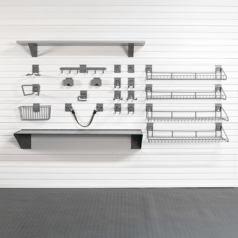 A set of dark gray metal wall-mounted shelves, baskets, and hooks arranged on a white slatwall in a clean indoor setting with a gray floor.