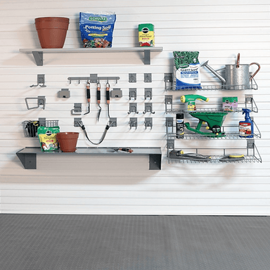 A wall-mounted garage organization system with two gray metal shelves, hooks, and wire racks holding gardening tools and supplies, including a terracotta pot, soil bag, seed bag, watering can, spray bottle, and hand tools, against a white paneled wall and gray garage floor.