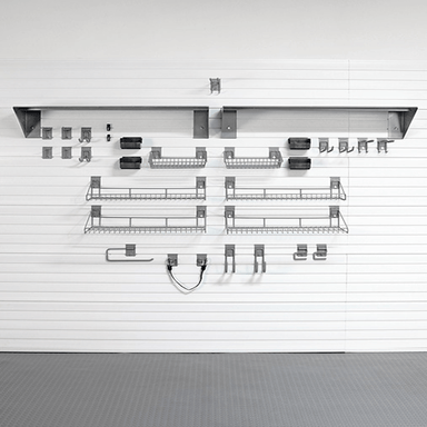 A set of gray metal wire kitchen shelves and hooks mounted on a white slatted garage door, with a gray floor visible below.