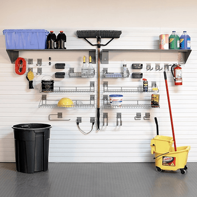 A garage wall organizer setup with a white slatwall, metal shelves, hooks, and various cleaning and storage tools including a broom, mop bucket, trash can, and storage bins.