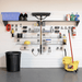 A garage wall organizer setup with a white slatwall, metal shelves, hooks, and various cleaning and storage tools including a broom, mop bucket, trash can, and storage bins.