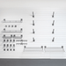 A set of dark gray metal wall-mounted shelving and hook accessories arranged on a white pegboard wall, with a dark gray floor visible at the bottom.