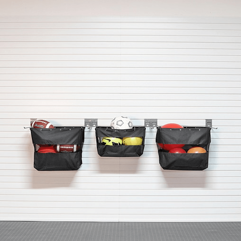 Three black fabric storage baskets hanging from a metal rack on a white paneled wall, filled with sports balls and footballs.