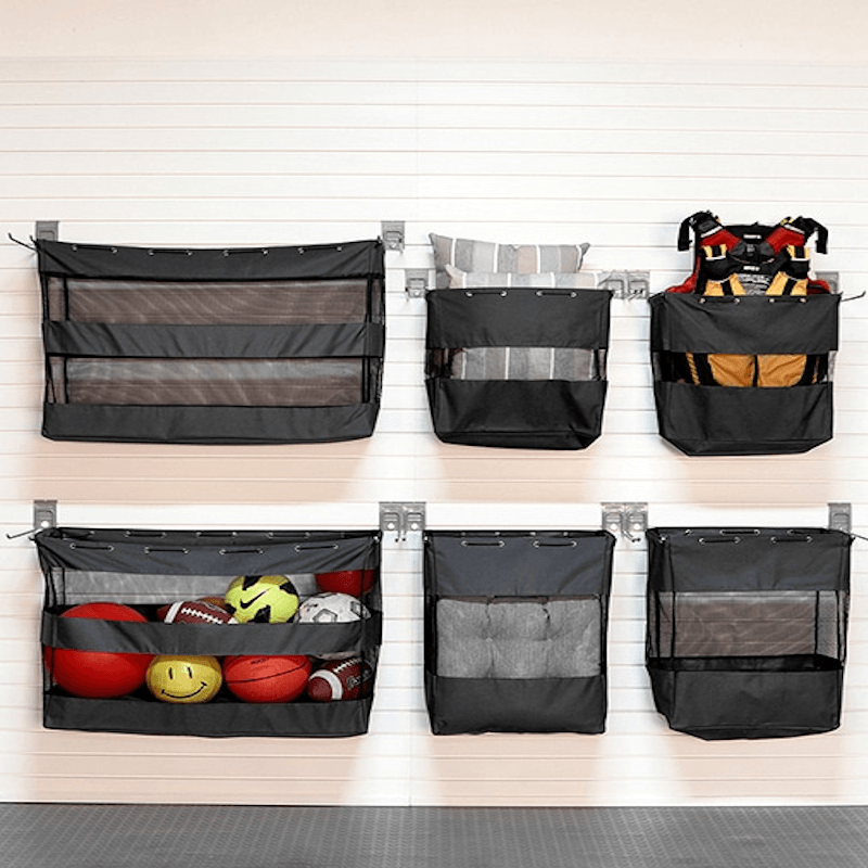 Six black mesh and fabric hanging storage pockets mounted on a white paneled wall, shown empty and filled with assorted sports balls and gear to demonstrate storage capacity.