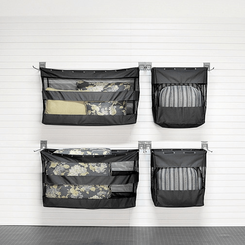 Four black mesh hanging organizer pockets mounted on a white paneled wall, each holding folded bedding or striped fabric items.