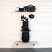 A black golf bag holding golf clubs is mounted on a white slatted wall above a gray shelf, with a black cap hanging to the right and a wire shelf above holding accessories.