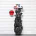 A black and navy golf bag hanging from a wall-mounted rack, with golf clubs inserted, a red Titleist cap on the left, and a small shelf holding golf accessories above.