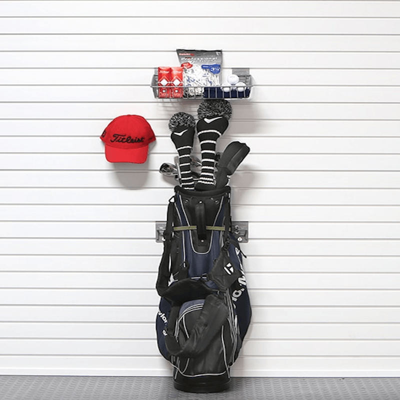 A black and navy golf bag hanging from a wall-mounted rack, with golf clubs inserted, a red Titleist cap on the left, and a small shelf holding golf accessories above.