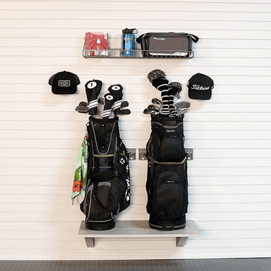 A wall-mounted golf bag rack holding two black golf bags with club heads and tees, plus a top shelf with a water bottle, pouch, and hat, against a white paneled wall.