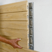 Light wood acoustic wall panels with a metal mounting bracket attached to a white wall, and a hand pointing at the panel profile.