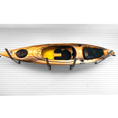 A sit-on-top kayak with a brown and gold wood-grain pattern and a bright yellow interior, mounted on a black wall rack against a white garage door.