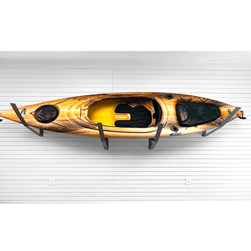 A sit-on-top kayak with a brown and gold wood-grain pattern and a bright yellow interior, mounted on a black wall rack against a white garage door.