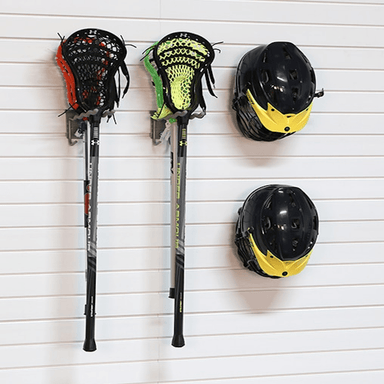 Two lacrosse sticks with attached lacrosse heads and two black lacrosse helmets with yellow accents, mounted on a white slatted wall.