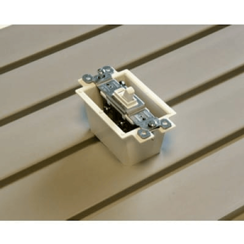 A close-up of a white electrical outlet cover or switch component with metal contacts, placed on a beige slatted surface.