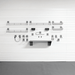 A set of wall-mounted metal storage shelves and hooks arranged on a white paneled wall above a gray floor.