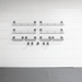 A set of dark gray metal wire baskets and hooks mounted in a grid pattern on a white paneled wall above a gray floor.