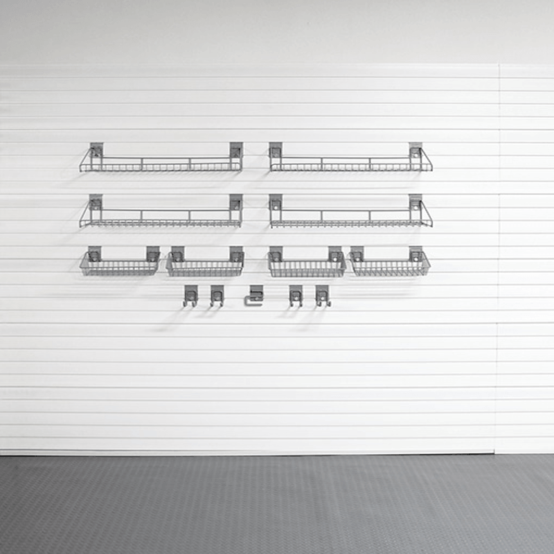 A set of dark gray metal wire baskets and hooks mounted in a grid pattern on a white paneled wall above a gray floor.