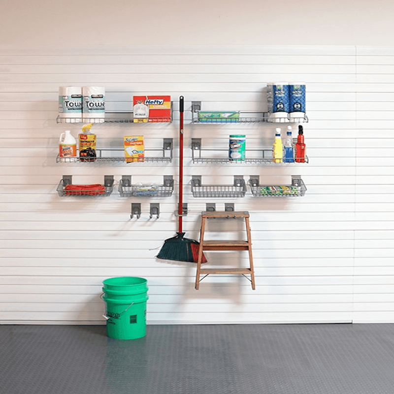 A wall-mounted metal garage organizer rack system with multiple shelves and hooks, shown installed on a white paneled garage wall. The rack holds assorted household cleaning products, a broom, a small wooden step ladder, and a green bucket on the floor.