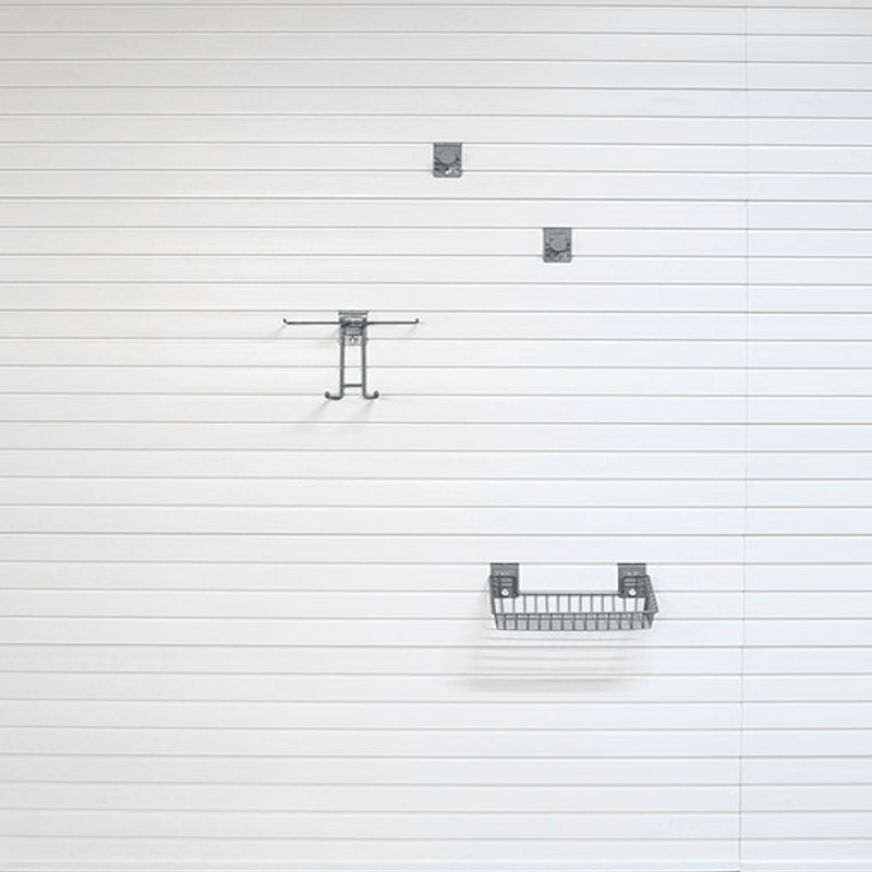 A minimalist set of three dark gray metal wall-mounted storage accessories, including two small square hooks and one wire basket shelf, arranged vertically against a white paneled wall.