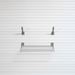 A metal wire shelf with two wall mounting brackets, shown against a white slatwall background.