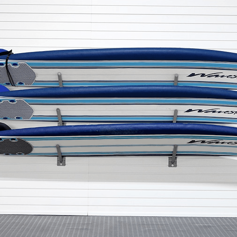 Three blue and white stand-up paddleboards mounted on a wall rack against a white paneled wall.