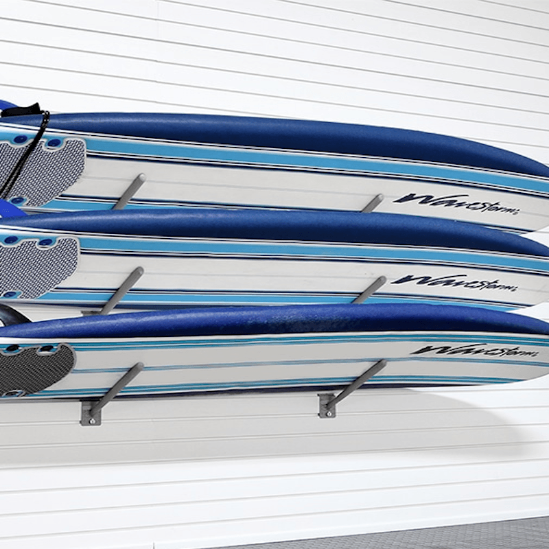 Three blue and white stand-up paddleboards mounted on a white slatted wall rack. The boards feature the brand name 'WaveStream' printed in black on their sides.