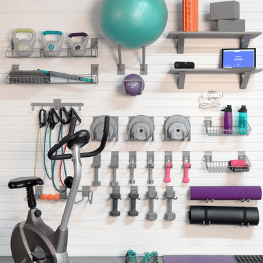 Staged home gym area utilizing the Deluxe Bundle, showing medicine balls, yoga mats, and weights organized next to a power strip for charging devices.